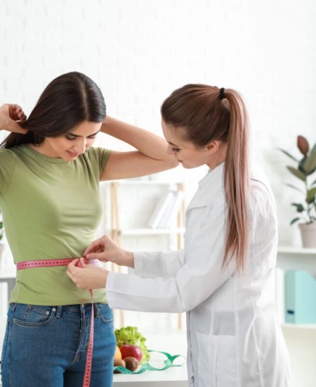 Nutritionist measuring waist of young woman in weight loss clinic